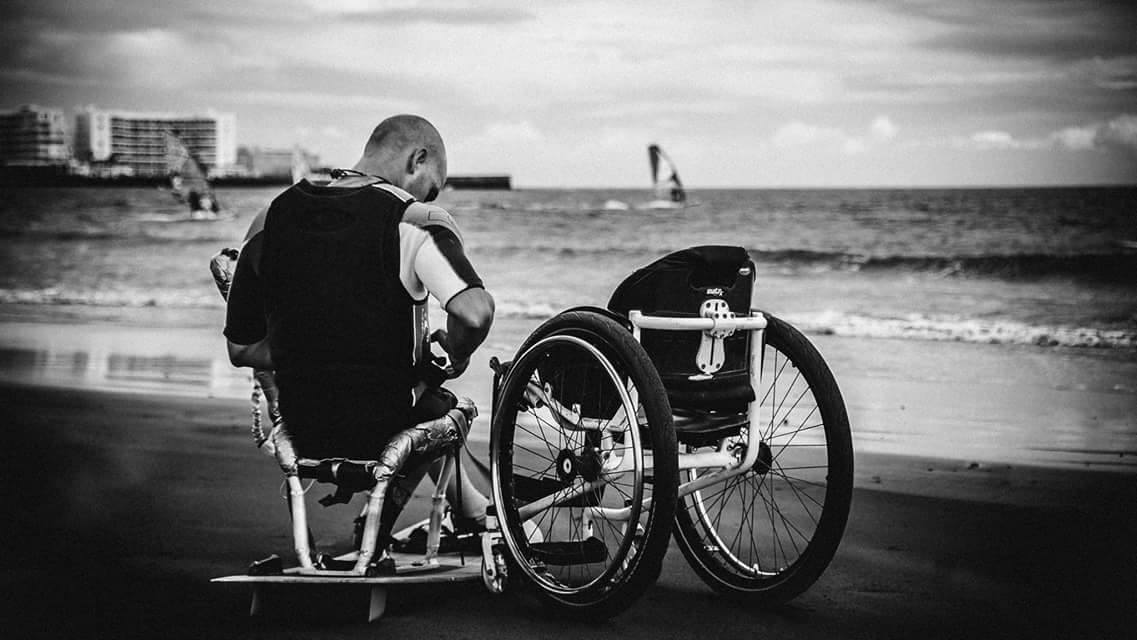 Man in a sitkite-board and a wheelchair to his right.
